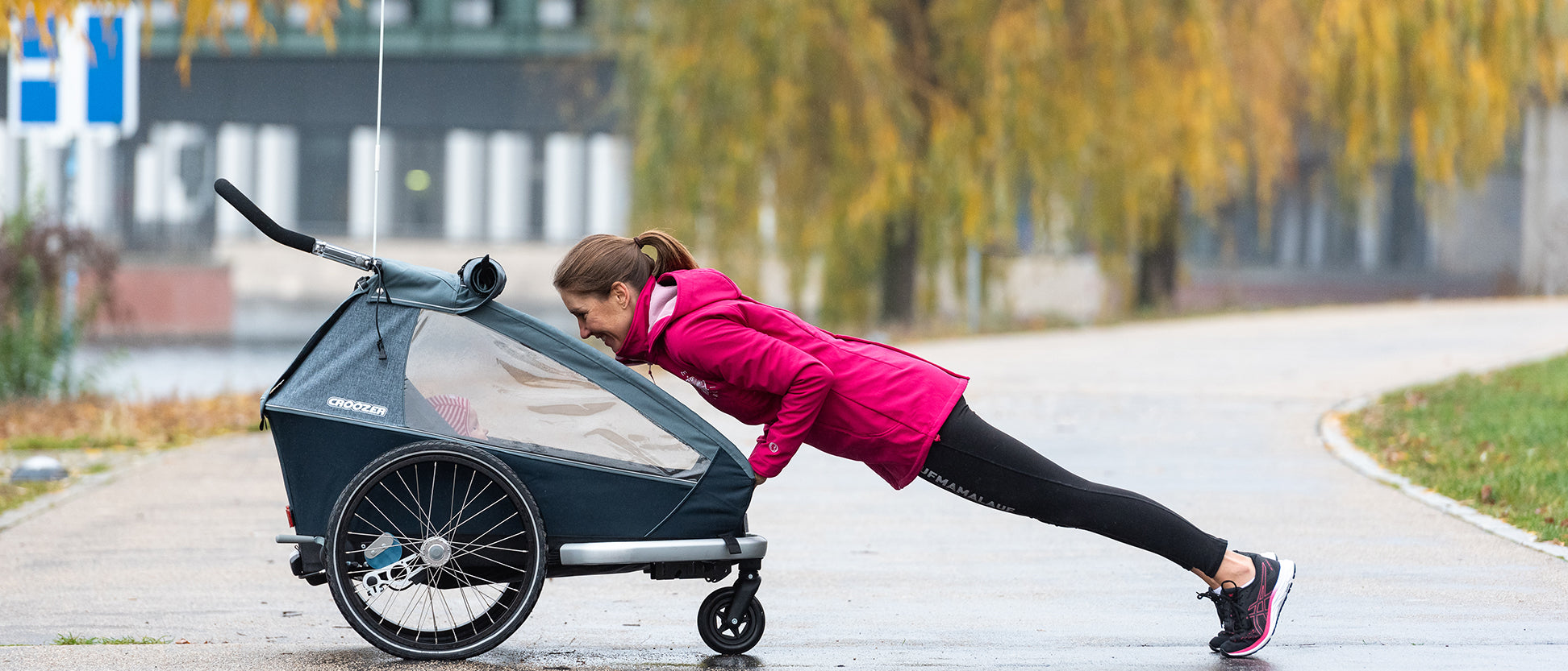 Woman in plank position using Croozer bike trailer for support during outdoor fitness workout in autumn